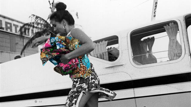Black and white image of Lilly Pulitzer running off plane with fabrics in her hand